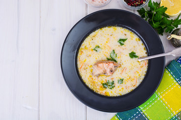 Creamy soup with salmon in black plate on white wooden table