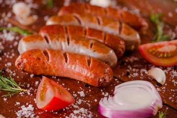 Close up of grilled sausages and vegetables, tomato and onion on a wooden background in rustic style