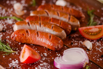 Close up of grilled sausages and vegetables, tomato and onion on a wooden background in rustic style