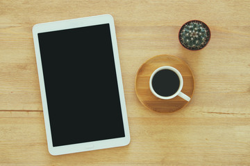 Tablet device with black screen next to cup of coffee over wooden desk.