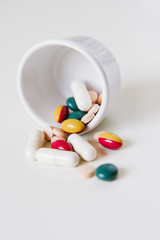 Various vitamin pills, medical capsules, supplements and drugs in tablet form in white, green, yellow, red and apricot on white background