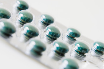 Green round medicine pills, supplements, vitamins or drugs in blister packaging on white table
