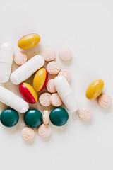Various vitamin pills, medical capsules, supplements and drugs in tablet form in white, green, yellow, red and apricot on white background