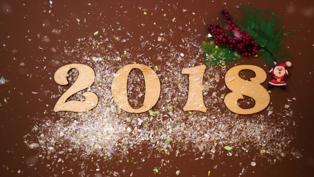 Christmas decoration and numbers 2018 on the brown table background the snow is falling from above. On the table are feather, rowanberry, santa, numbers 2018 and snow.Top view.