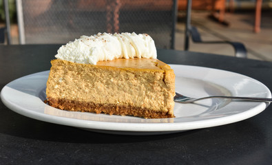 Plated dessert of golden pumpkin cheesecake, whip cream with nutmeg powder, fork,
