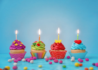 Festive bright cupcakes with candles on color background