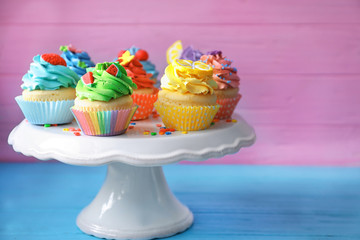 Stand with tasty bright cupcakes on color background