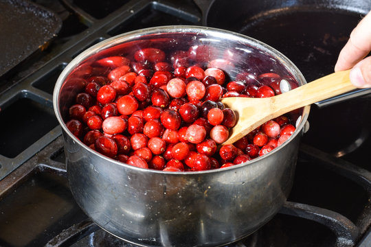Cooking fresh red cranberries fto make cranberry sauce for Holiday dinner.  Wooden spoon stirs berries in stainless steel pot.