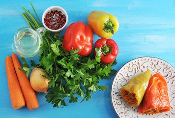 Bell peppers stuffed with carrot and herbs and ingredients on blue wooden background