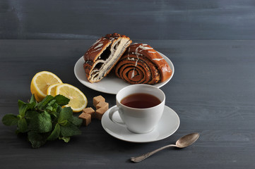 roll with poppy seeds, tea, lemon and mint on wooden background