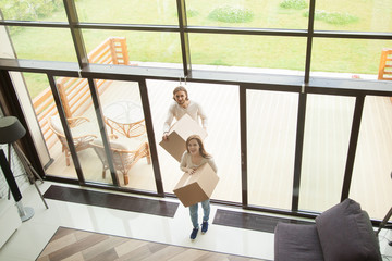 Excited couple holding boxes entering new house on moving day, happy man and woman coming into modern home with glass wall, family relocating in beautiful building with terrace, top view from above