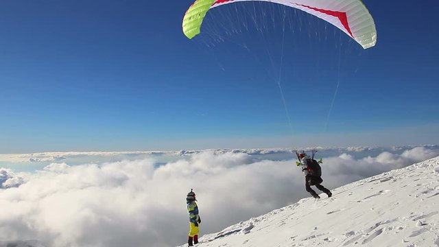 Paragliding above mountain peaks and clouds during winter sunny snowy day