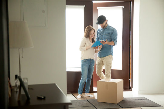 Young woman putting signature receiving cardboard box from courier at home, receiver singing document for accepting parcel, man delivering package to customer, door delivery service concept