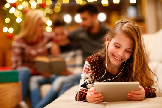 little girl with headphones is using a tablet and smiling.