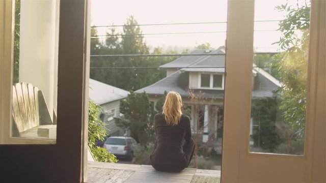 zooming shot of a young athletic woman with blonde hair sitting on her porch, on a sunny day