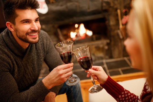 couple in love sitting on floor at burning fireplace and drink wine.