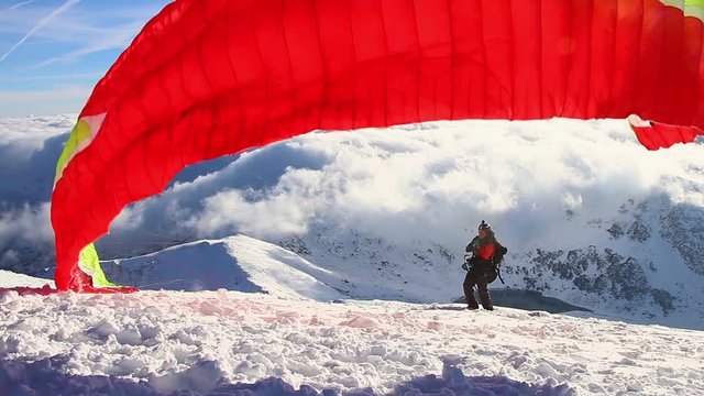 Paragliding above mountain peaks and clouds during winter sunny snowy day