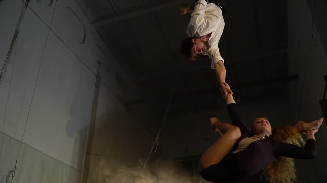 A strong man hangs upside down and holds a flexible woman with an aerial acrobat, slow motion