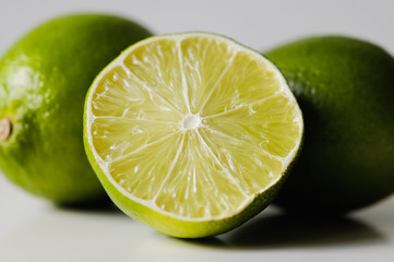 Close up shot of halved key lemon lime with two limes in background on whtie background