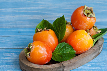Fresh ripe persimmons in a bowl on a wooden table. Close-up.