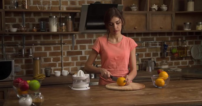 Woman prepares fresh orange juice at home kitchen 4k video. Female cutting citrus fruit and squeezing out juice on juicer squeezer. Extracting  juicing healthy drink beverage