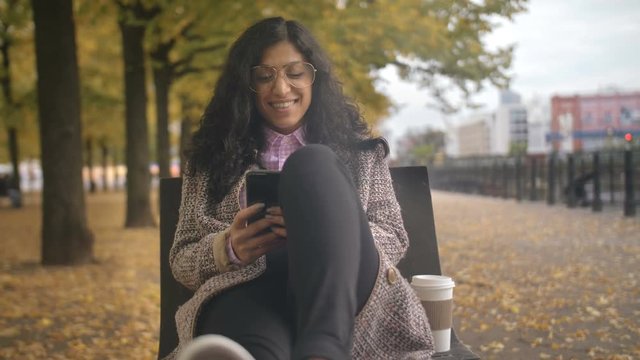 women's thoughts and dreams multiracial girl on a bench in an autumn park touches the smartphone screen and writes a chat message