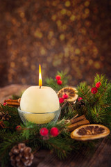 Close up round ivory burning Christmas candle on advent wreath with natural decor on the old rustic table with blurred luminous background. Christmas festive concept. Selective focus. Space for text