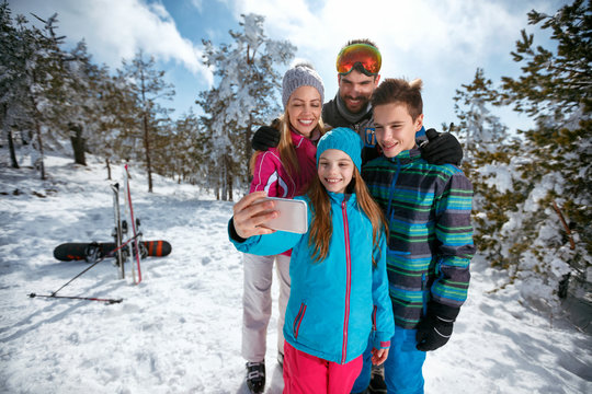 family smiling and making selfie with mobile on winter ski vacation