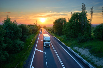White truck and red one driving on the highway in a rural landscape at sunset. View from above.