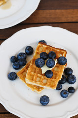 Homemade traditional Belgian waffles with fresh blueberries and butter on white vintage plate on wooden balcony table served as a sweet breakfast dish or snack