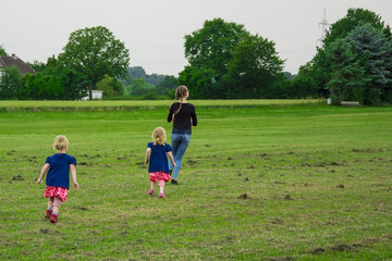 children fun running around the green field. two girls play with their older sister