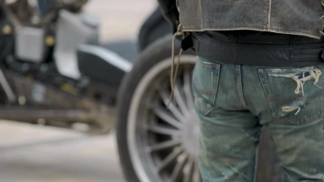 Man with brown boots and ripped jeans standing next to motorcycle, tough biker