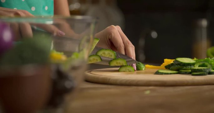 Woman hand prepares salad at home kitchen 4k close-up video. Female cooking side dish: cutting cucumbers, knife slicing, vegetables on table. Healthy food 