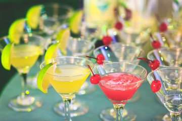 Beautiful line of different coloured cocktails on a party, tequila, martini, vodka, and others on decorated catering bouquet table on open air party, tropic beach hawaiian party setting