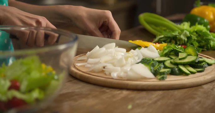 Woman hand prepares salad at home kitchen 4k close-up video. Female cooking side dish: cutting onion, knife slicing greenery, vegetables on table. Healthy food