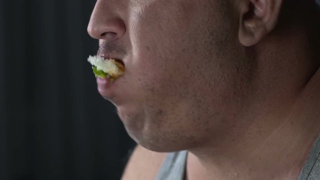 Closeup of a plump guy eating hamburger, psychological problems of overeating