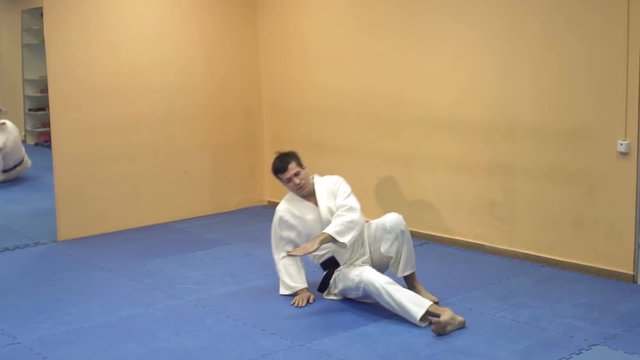 A man in a kimono demonstrates a somersault through himself in the gym. Man doing aikido.