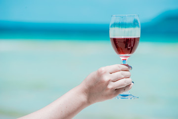 Young Asian woman wearing Hawaiian with hat and sunglasses is happy when they go to the beach for a holiday. Drinking a glass of wine together.