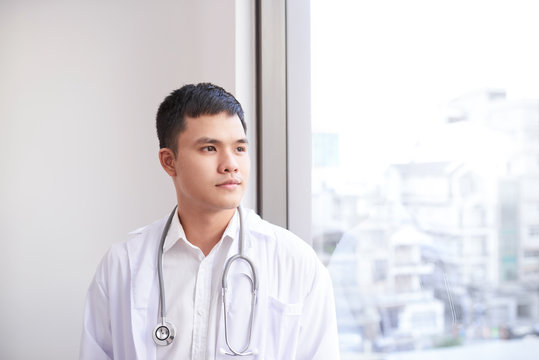 Young Male Asian Doctor Looking Out Of The Window At Hospital