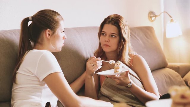 Two young women in plaide are watching TV and warming with tea at home.

