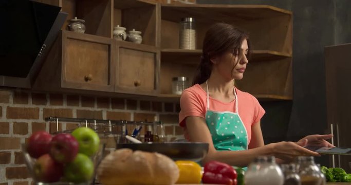 Woman cooking with tablet on home kitchen modern interior 4k video. Female reading preparing recipe and frying omlette or pancakes