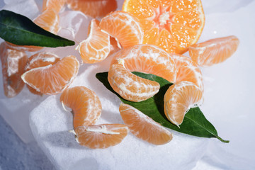 Fresh orange mandarin fruit with green leaves are frozen on cold blue ice