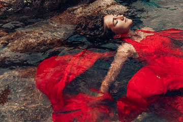 beautiful young woman in red dress laying dowm in water