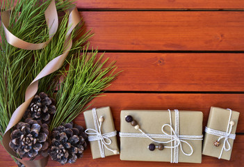 Christmas background, wrapped gifts, pine branch and cones, wooden surface as copy space.