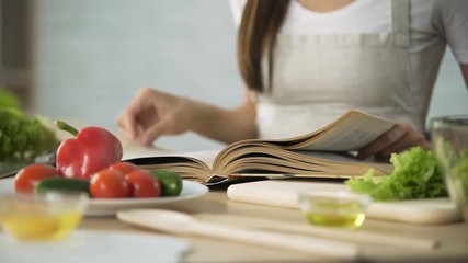 Close-up of girl flipping through cooking book pages, choosing salad recipe