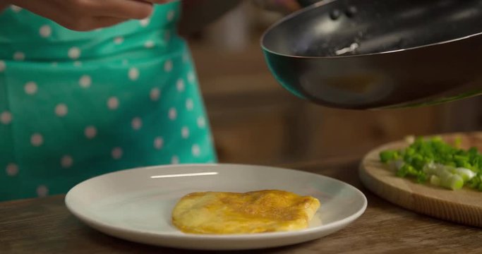 Woman hand prepares serving plate with omelette sprinkling green onion 4k video. Female cooking food at home kitchen: dish greenery and fried eggs, scrambled omelet on pan