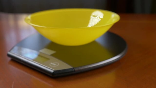 someone measures a piece of brown rice, on an electronic scale in the kitchen. pour the rump into a deep round bowl, standing on a flat weighing platform. 4k, slow motion, dolly shot