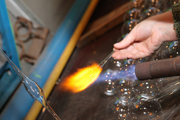 Factory of Christmas toys. The worker blows out the glass. The burner melts the glass. Decoration of a Christmas tree toy. Handmade. Manufacture of fur-tree toys. Many beautiful glass beads.