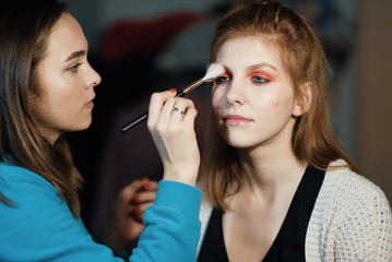 Makeup artist making make-up for a beautiful young woman at home 