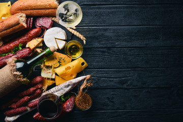 A bottle of wine, cheeses and traditional sausages on a wooden background. Brie cheese, blue cheese, gorgonzola, fuete, salami. Free space for text. Top view.